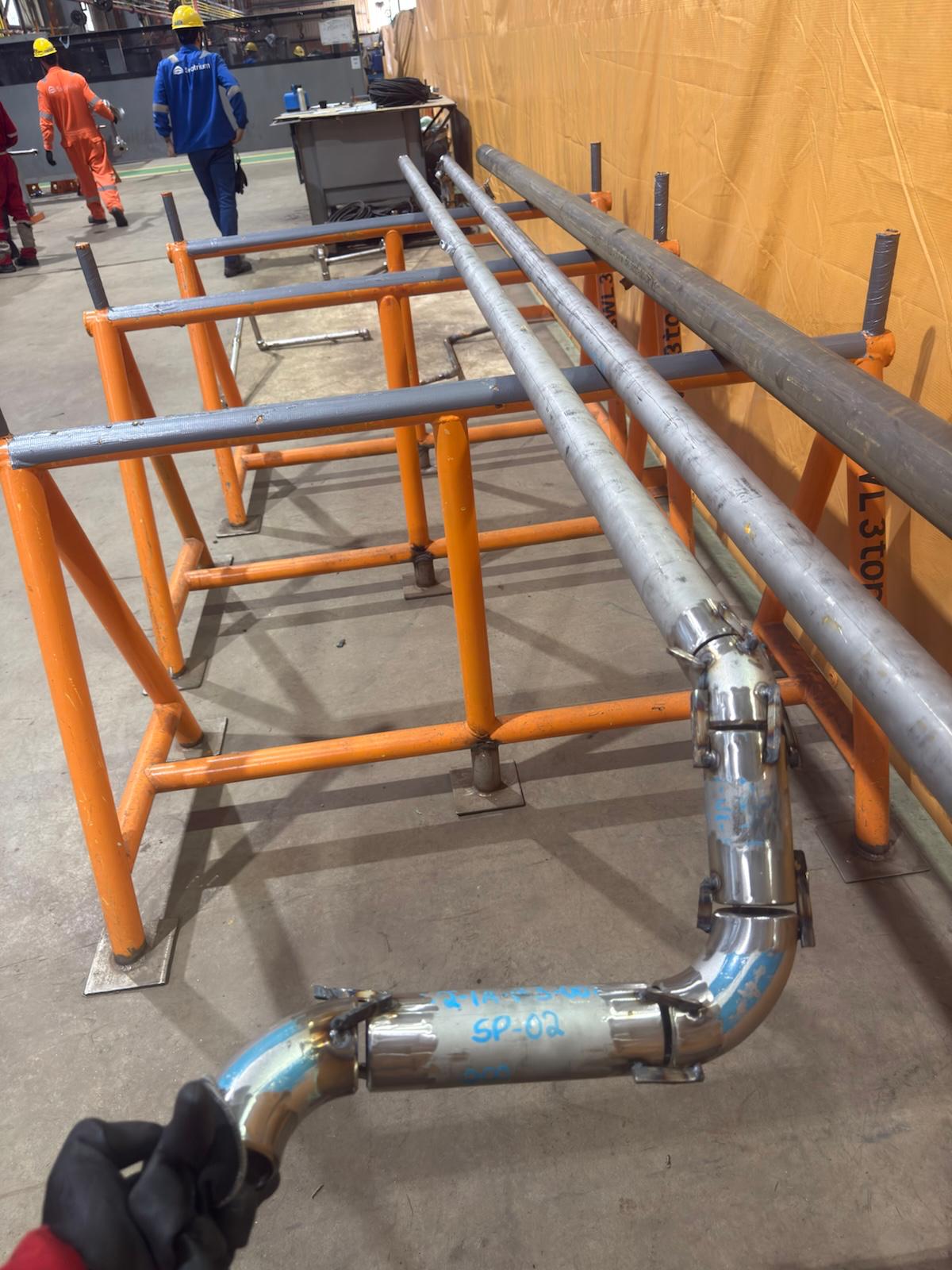 Tubos alinhados em cavaletes e spool de aço inox montado em canteiro industrial
